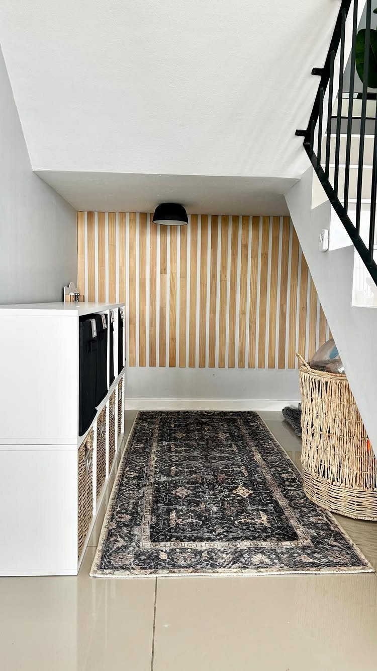 White storage cubbies with wicker baskets and a patterned rug under a staircase with wood slat walls.