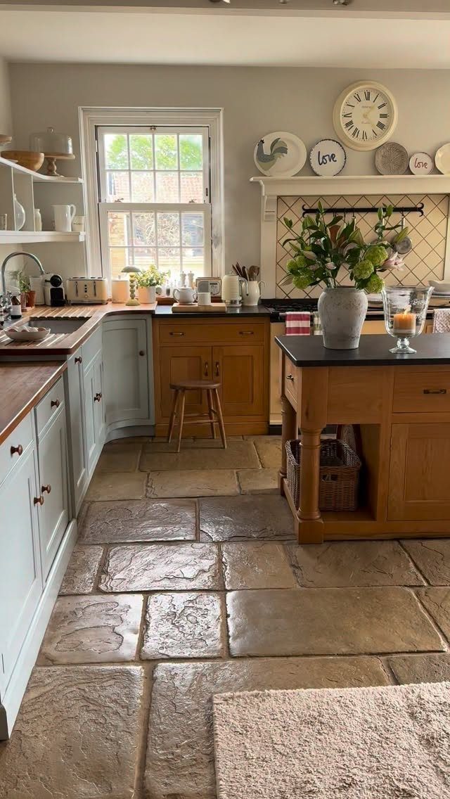 Rustic farmhouse kitchen with light blue cabinets, wooden countertops, and large stone floor tiles.