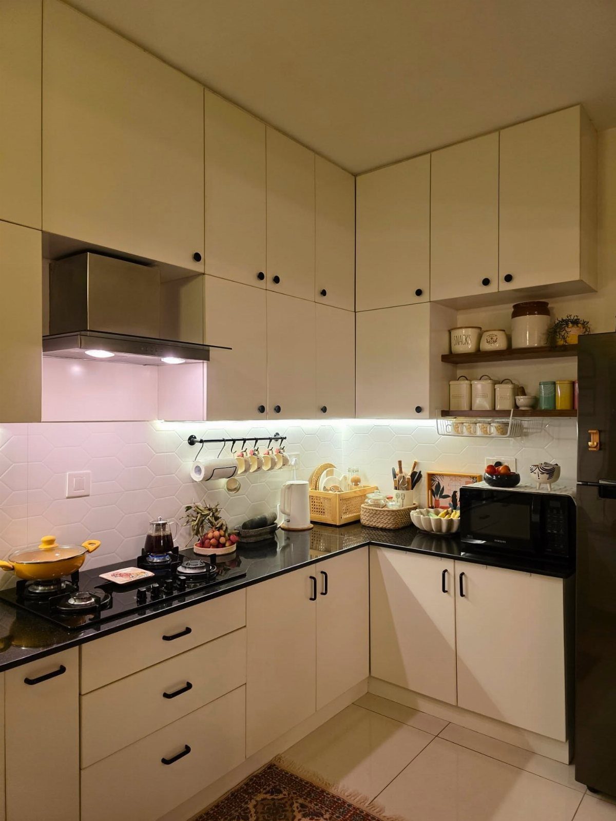 Cream kitchen cabinets with black countertops and white tiled backsplash in an L-shaped layout.