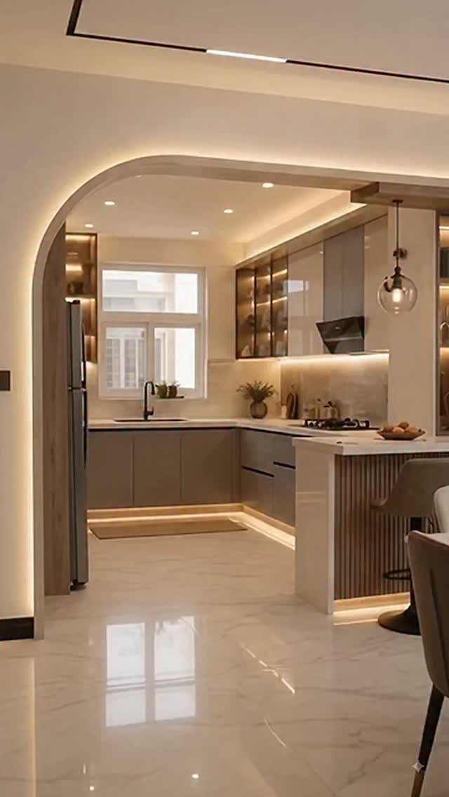 Modern kitchen with grey cabinets and warm lighting seen through a large arched doorway.