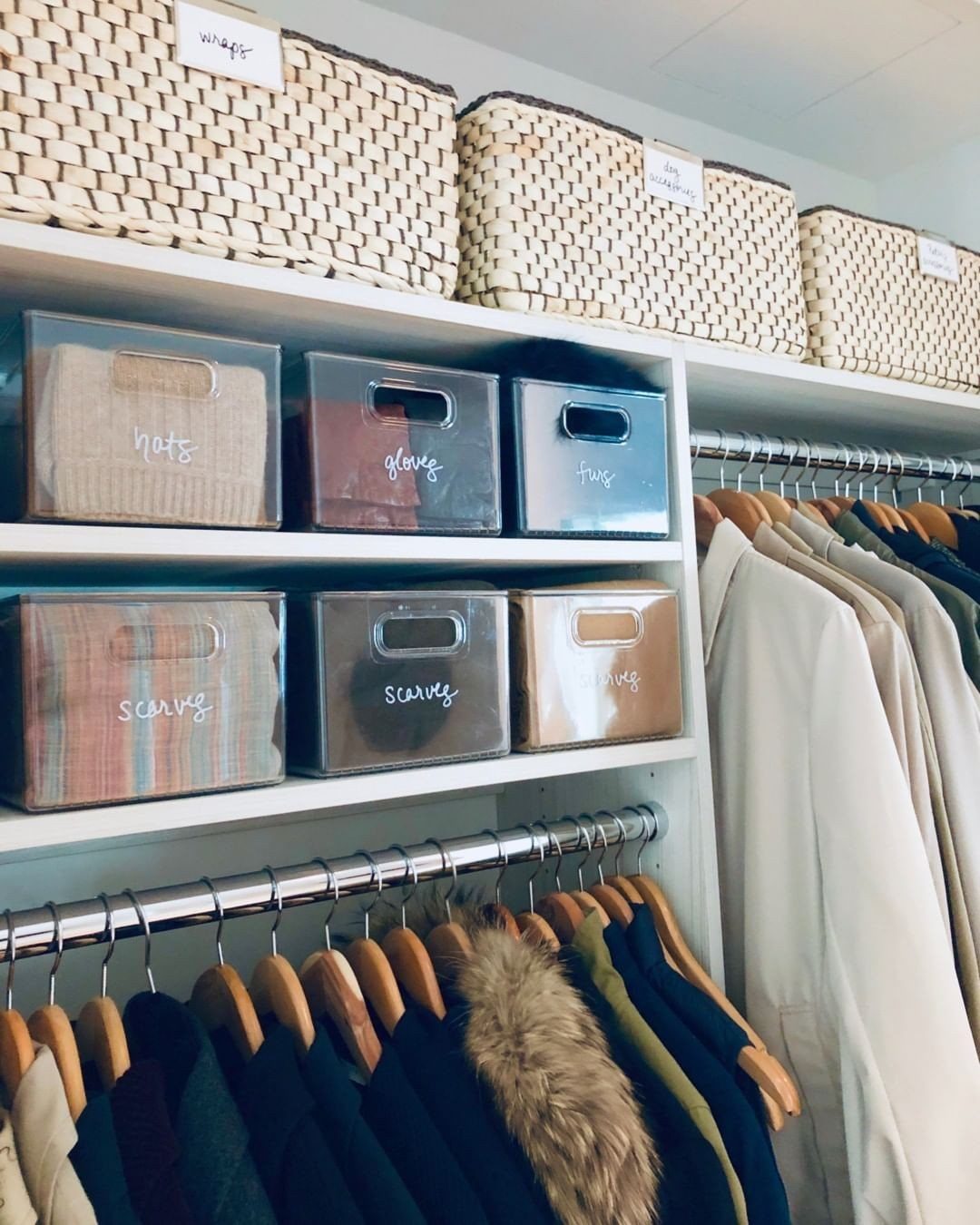 11 Ideas to Organize a Closet for Maximum Storage 5 Woven baskets and labeled clear plastic bins organized on white closet shelves above hanging clothes.
