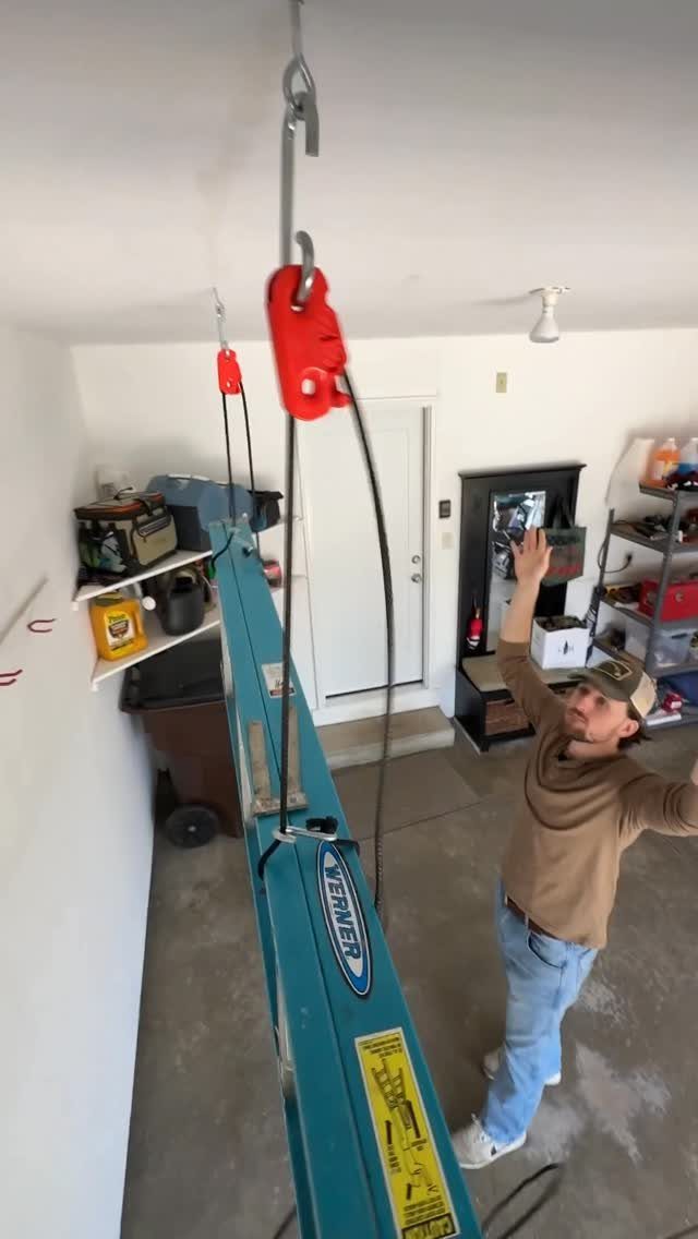 22 Organize a Garage Ideas for Workbenches, Zones & Wall Systems 7 A man reaches toward a teal ladder being hoisted by a red pulley in a garage.