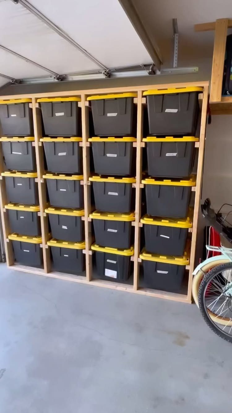 22 Organize a Garage Ideas for Workbenches, Zones & Wall Systems 3 Black storage bins with yellow lids arranged on a wooden shelving unit in a garage.