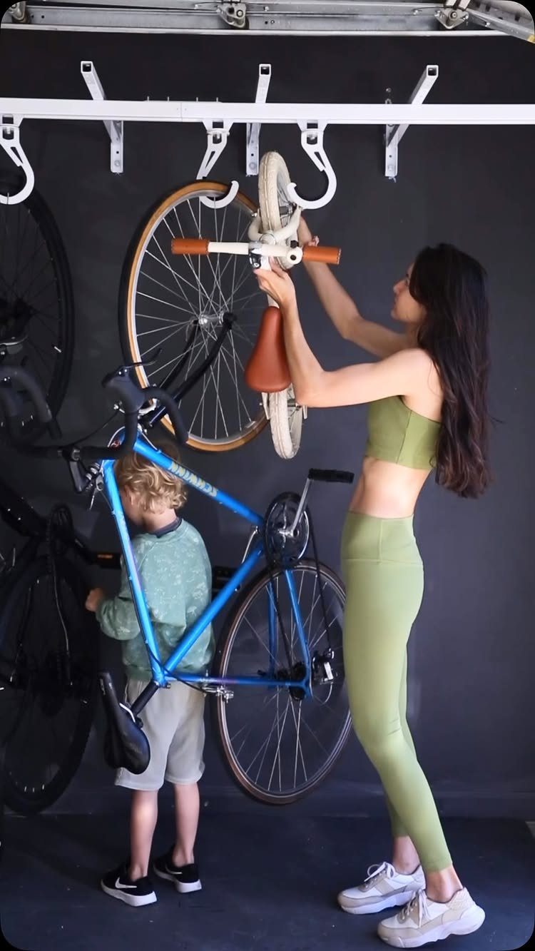 22 Organize a Garage Ideas for Workbenches, Zones & Wall Systems 10 A woman and child hanging a blue bicycle onto a white wall-mounted storage rack.