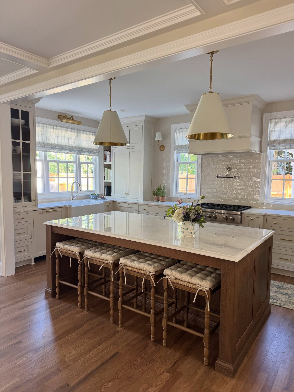 Large kitchen island with white marble countertop and four tufted wooden barstools on hardwood floors.