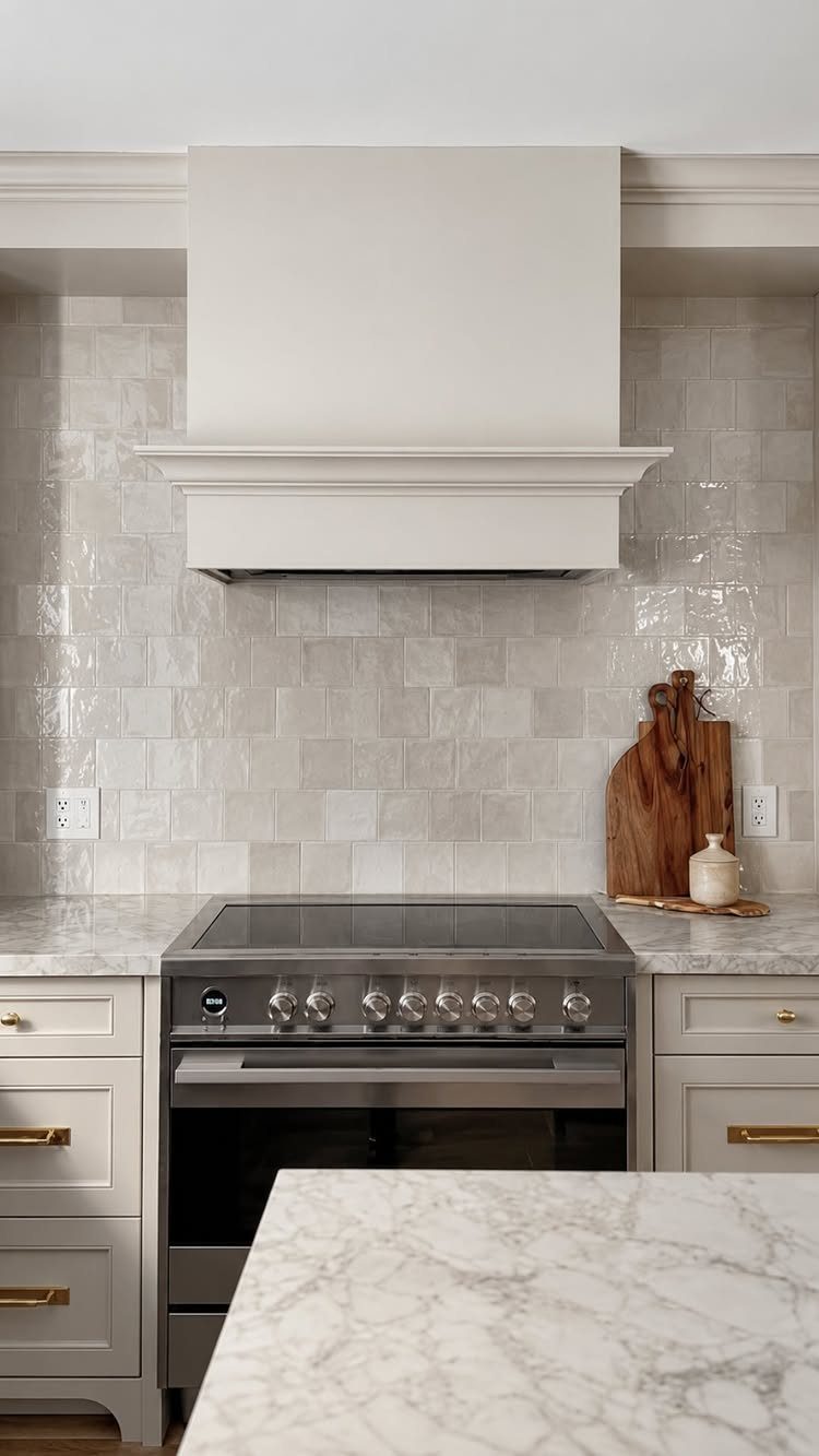 Light gray textured tile backsplash behind a stainless steel stove and white range hood.