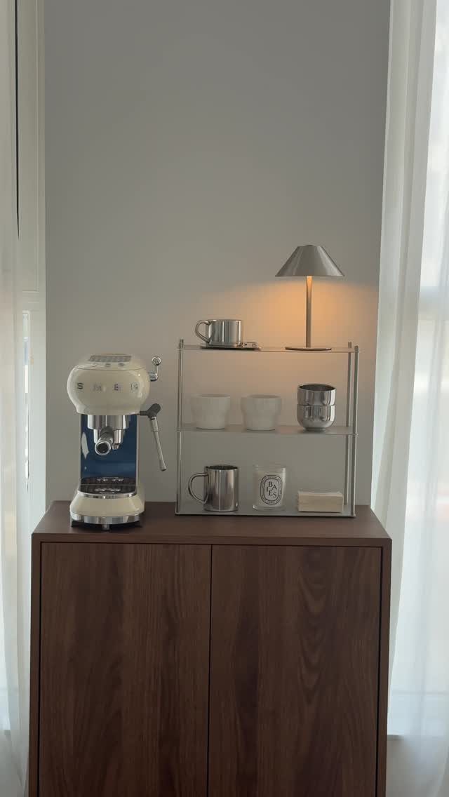 White espresso machine and clear acrylic shelf with coffee accessories on a wooden cabinet.