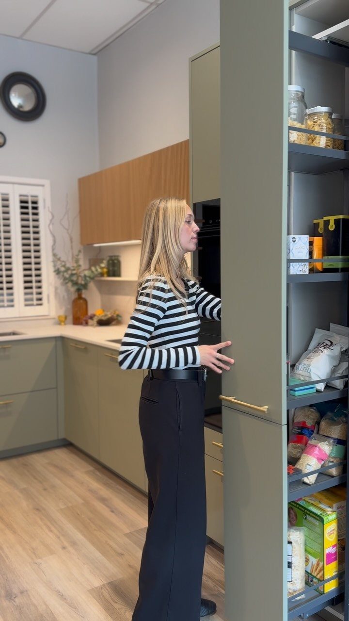 20 Simple and Small Kitchen Design Ideas 7 A woman stands next to an open, tall grey pull-out pantry filled with food items.