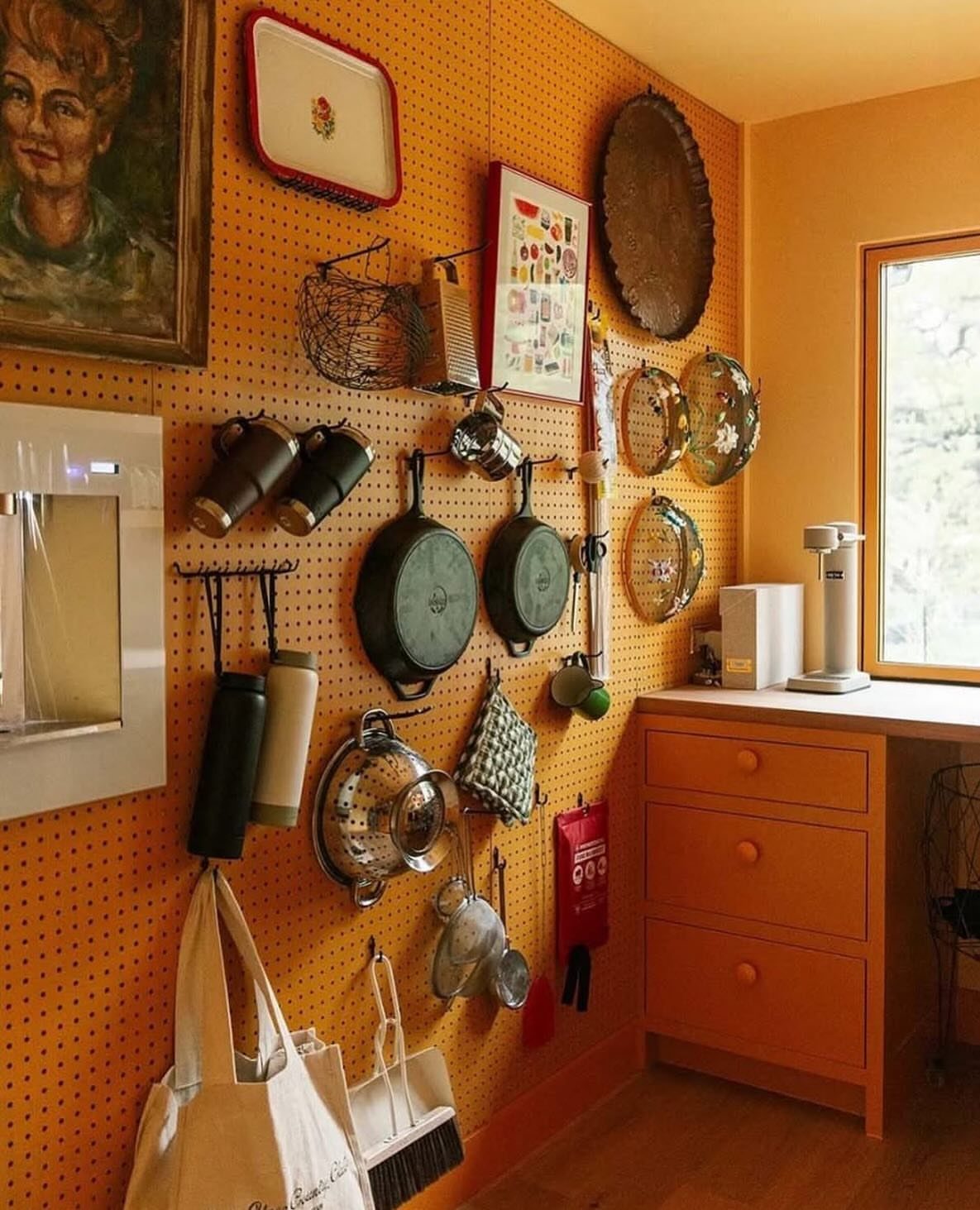 20 Simple and Small Kitchen Design Ideas 12 Orange pegboard mounted on a kitchen wall holding various cooking utensils and pans.