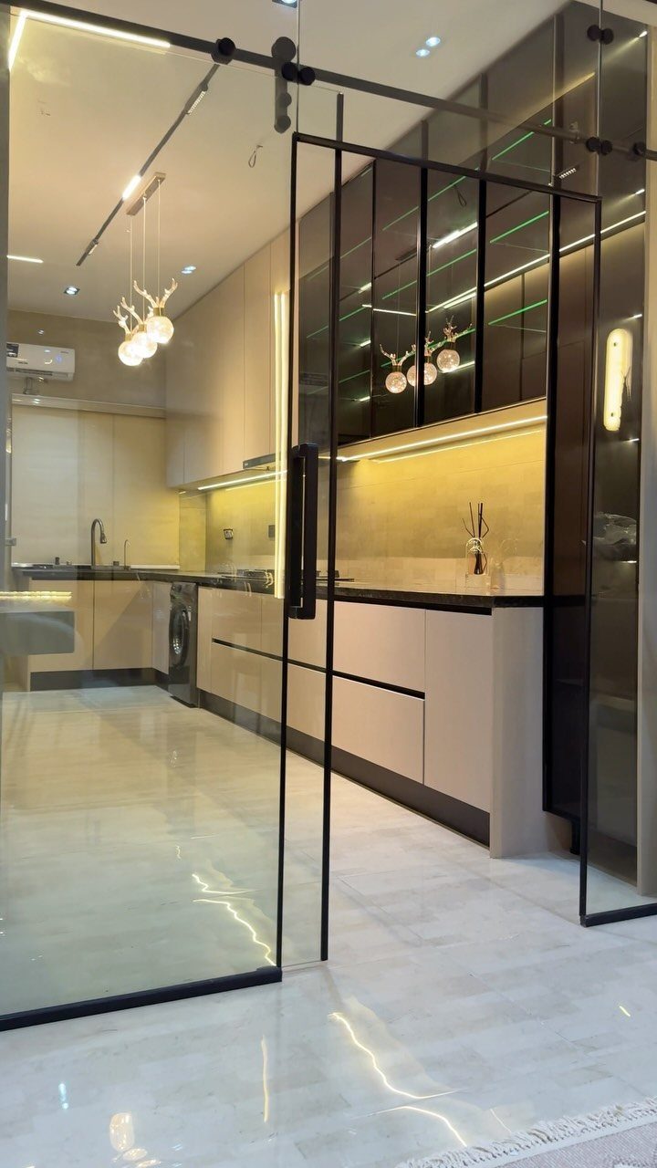 20 Sleek Kitchen Cabinet Design Ideas for 2026 8 Modern kitchen with beige cabinets seen through large black-framed glass sliding doors.