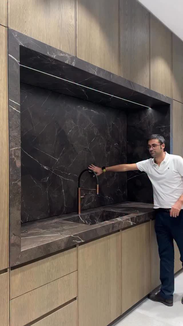 20 Sleek Kitchen Cabinet Design Ideas for 2026 19 Man standing beside a modern kitchen with light wood cabinets and dark marble backsplash.