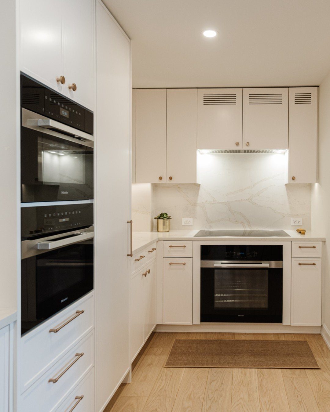 20 Sleek Kitchen Cabinet Design Ideas for 2026 13 White kitchen cabinets featuring slim gold hardware and integrated black appliances with marble backsplash.