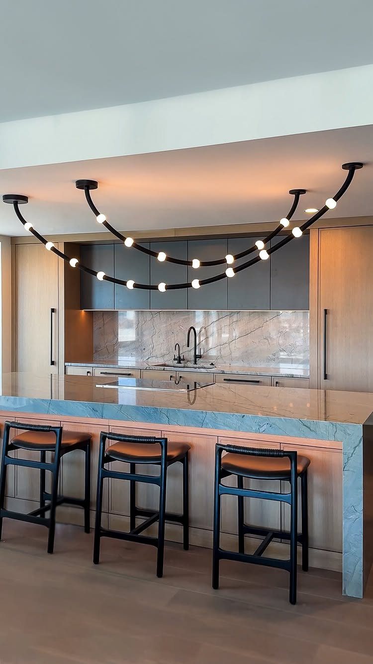 20 Sleek Kitchen Cabinet Design Ideas for 2026 3 A sculptural black light fixture with glowing bulbs hangs over a marble kitchen island.