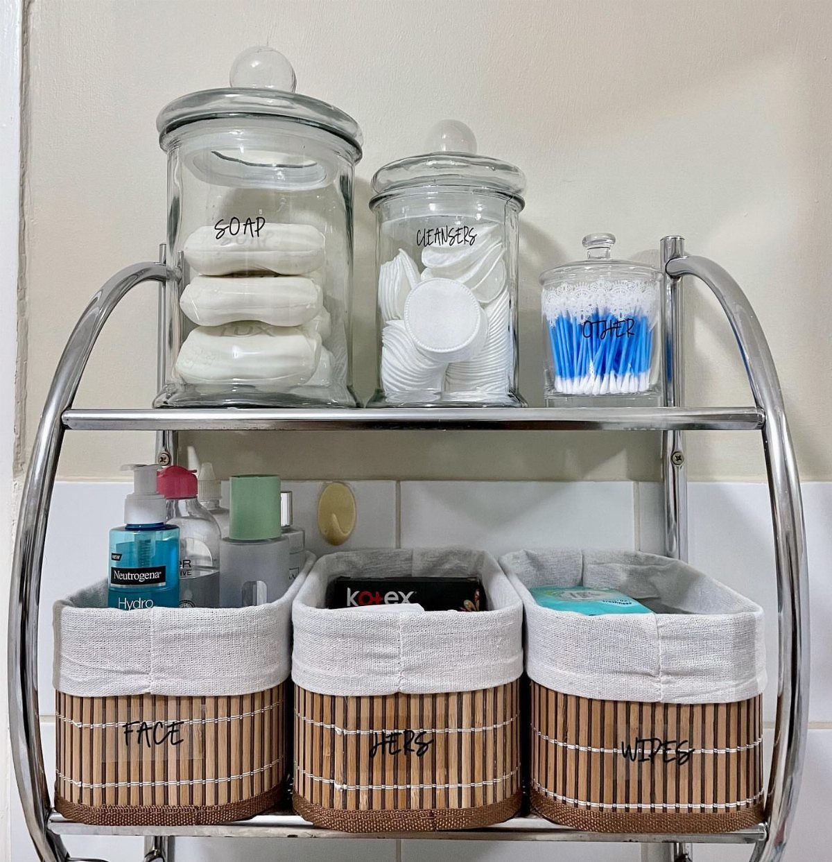 Three labeled woven baskets sit on a chrome shelf below glass storage jars.