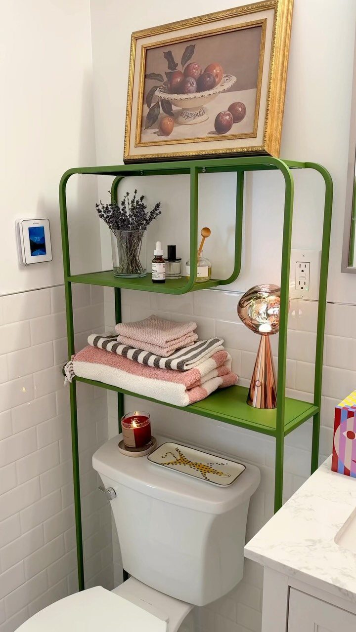 Green metal shelving unit positioned over a white toilet in a bright bathroom with subway tiles.