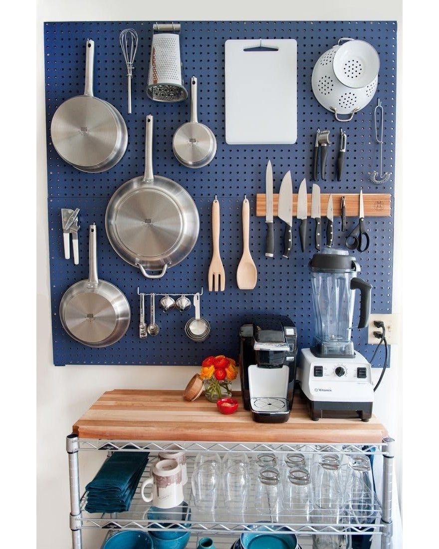 Stainless steel pans and kitchen utensils hanging on a blue pegboard above a wooden countertop.