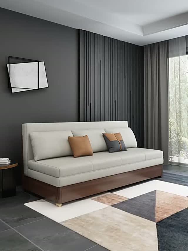 A slim beige sofa with decorative pillows sits on a geometric rug in a modern room.