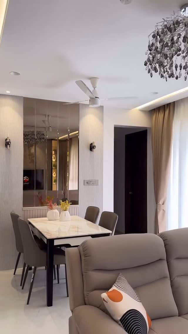 A marble dining table with grey chairs set against a large mirrored wall in a modern living room.