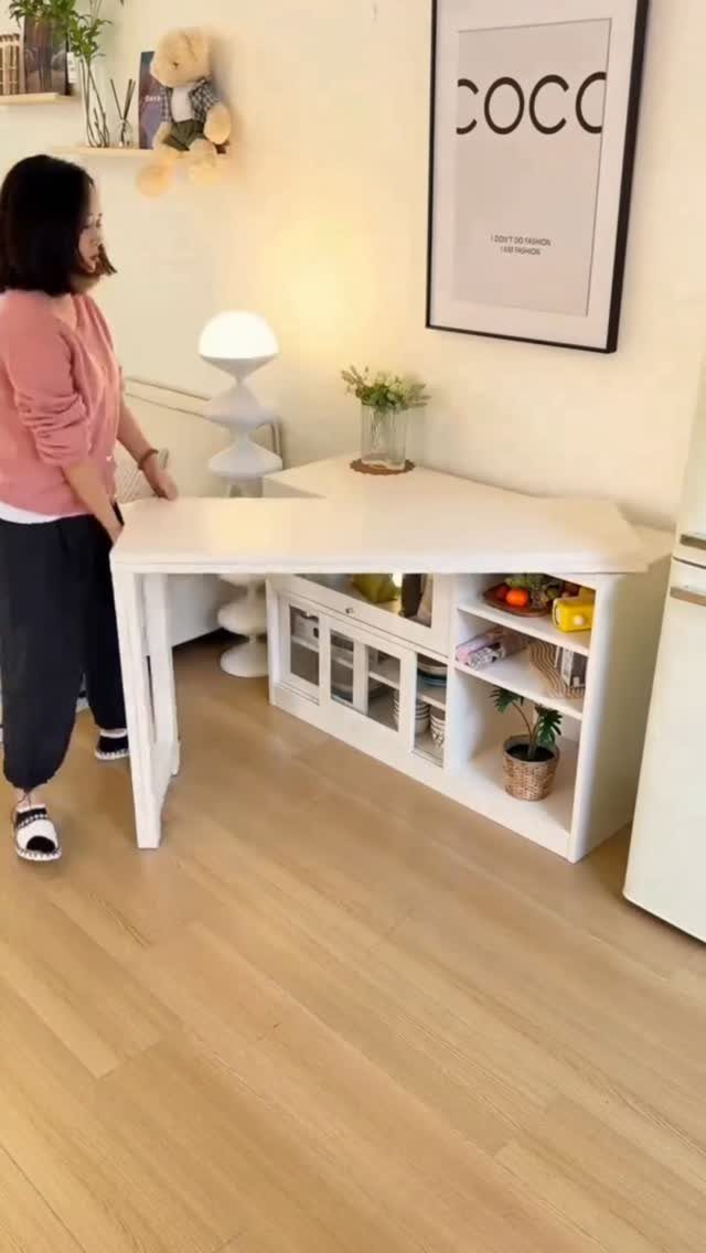 14 Small Apartment Storage Hacks and Genius Finds for 2026 11 A woman stands by a white extendable table with integrated storage shelves in a bright room.