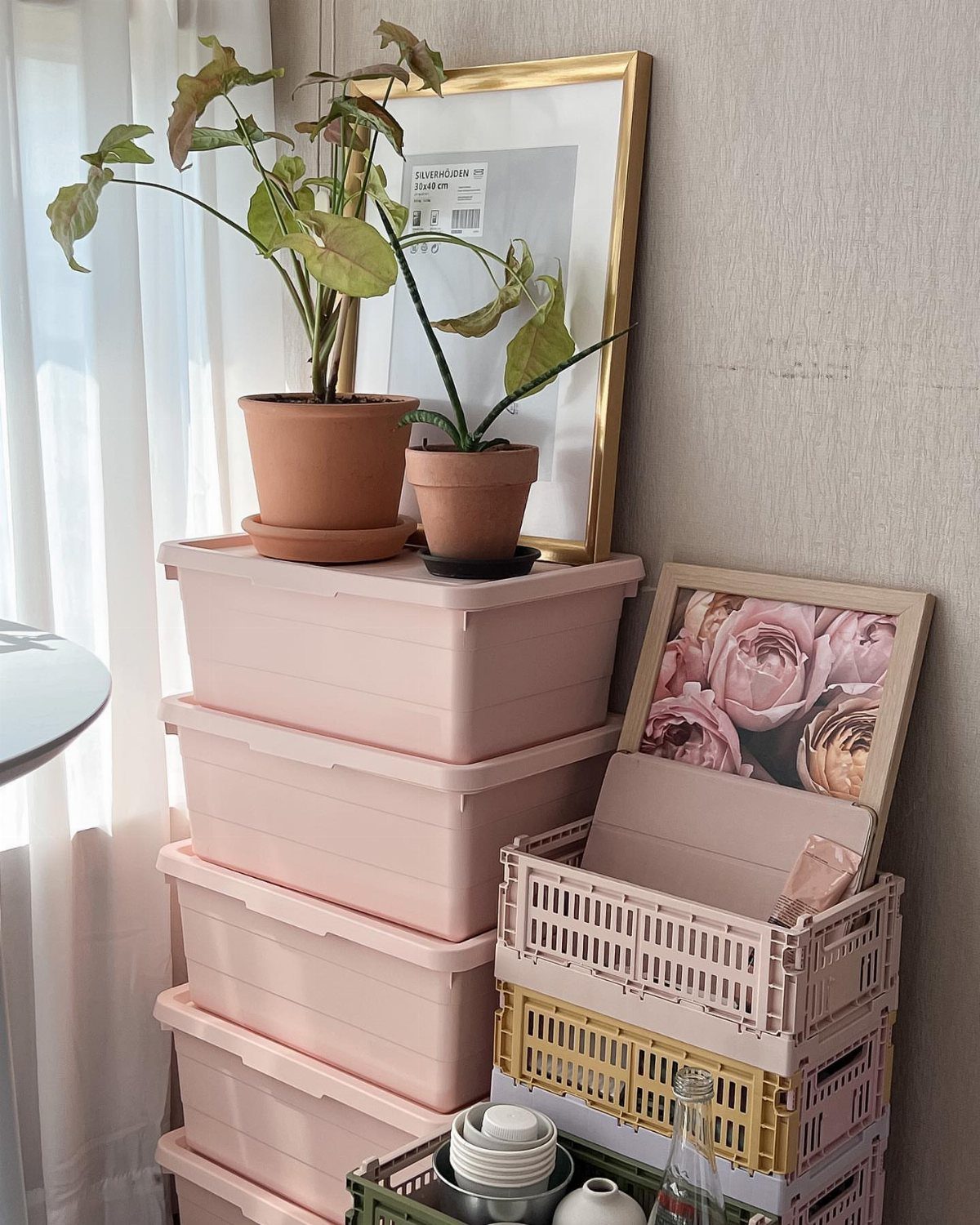 14 Small Apartment Storage Hacks and Genius Finds for 2026 7 Pink plastic storage bins stacked next to colorful crates and potted plants against a wall.