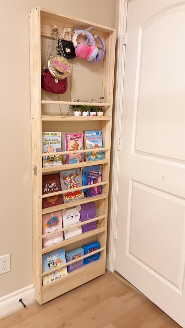 14 Small Apartment Storage Hacks and Genius Finds for 2026 14 A tall wooden shelving unit holding children's books, small plants, and hanging purses against a white wall.
