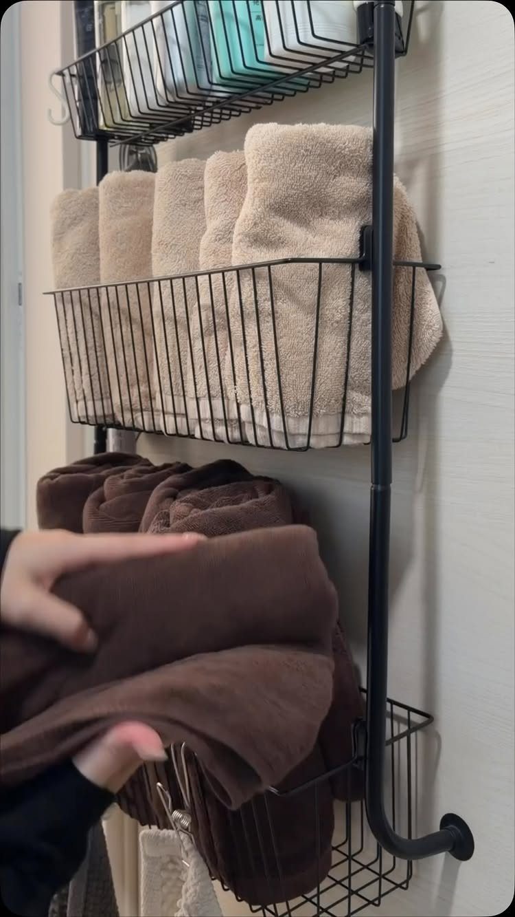 14 Small Apartment Storage Hacks and Genius Finds for 2026 13 Black wire shelving unit on a wall holding folded beige and brown towels.