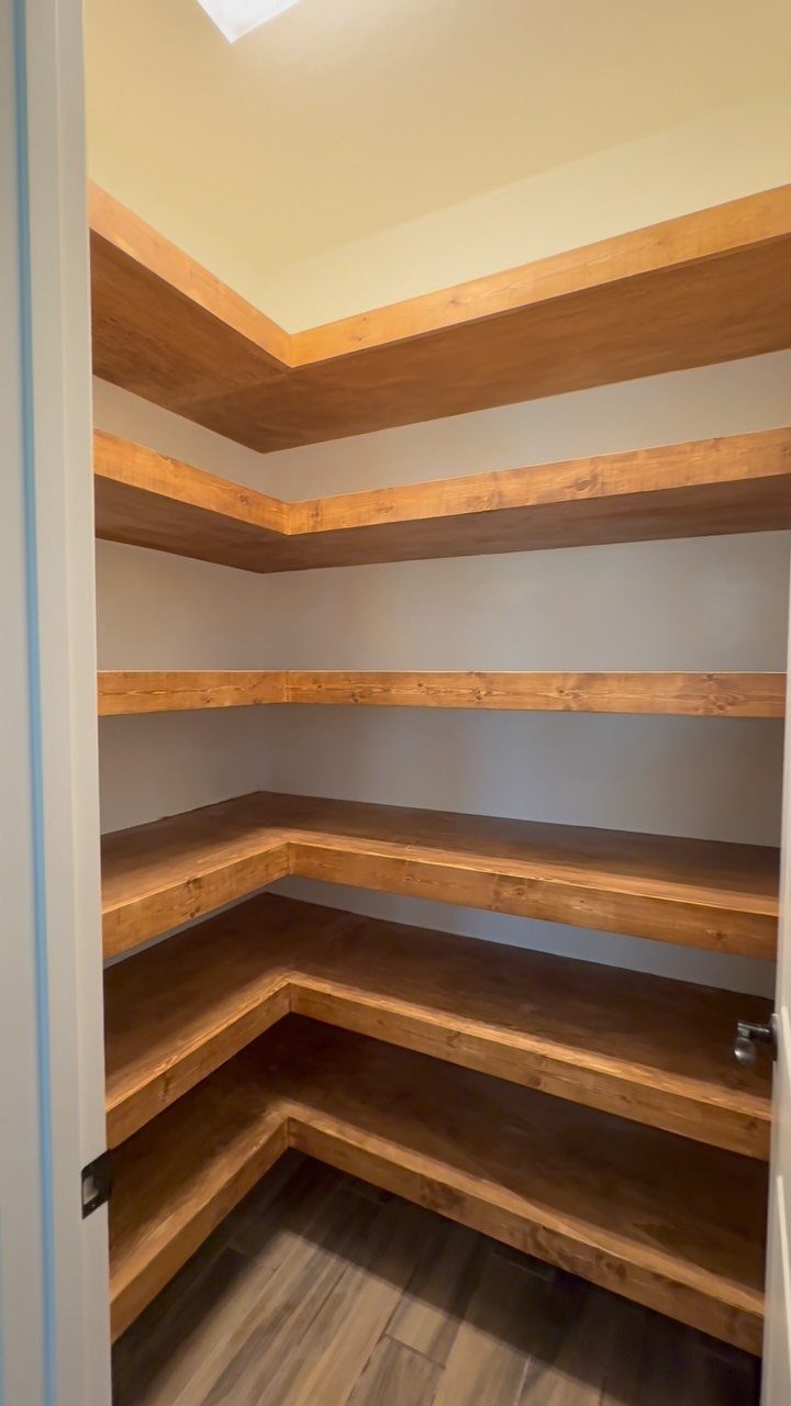 Empty wooden custom shelves installed in the corner of a small pantry with white walls.