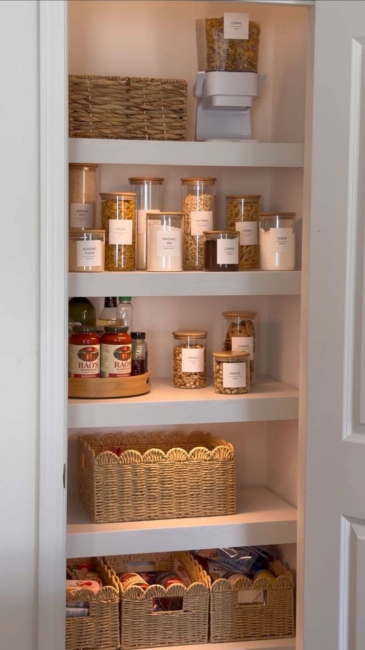 White pantry shelves holding labeled glass jars, wicker baskets, and organized food items.