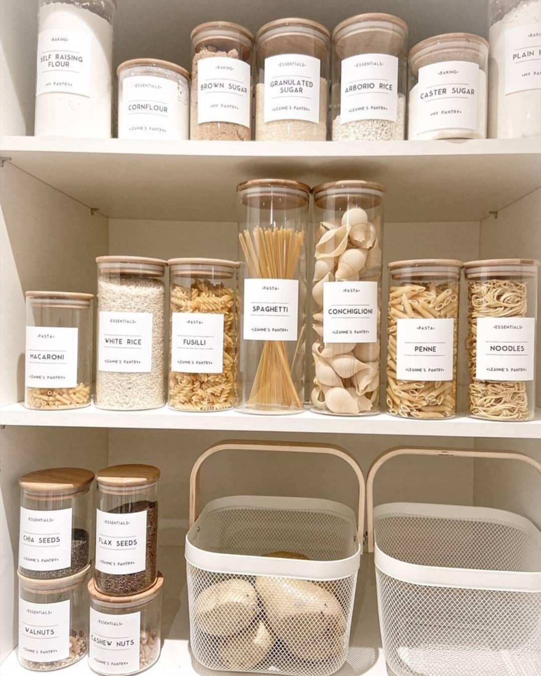 Clear pantry containers filled with various dry foods and neatly labeled with white stickers.