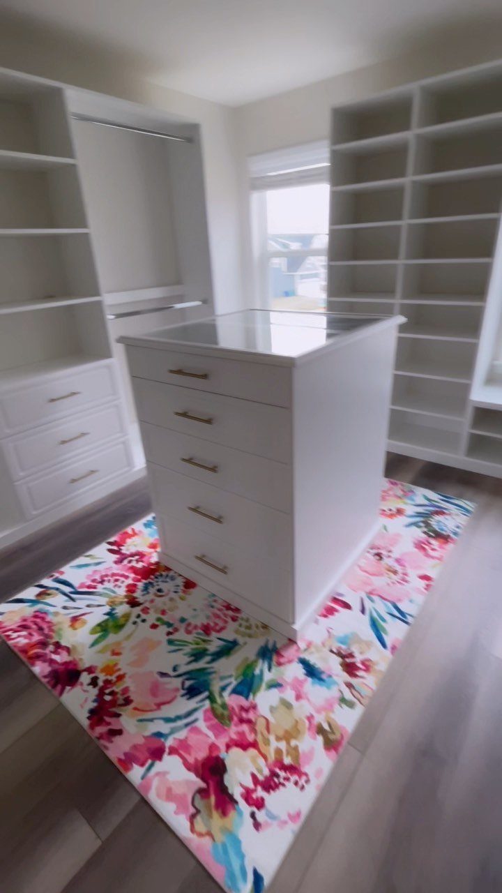 White built-in closet shelving and a central dresser island on a floral rug.