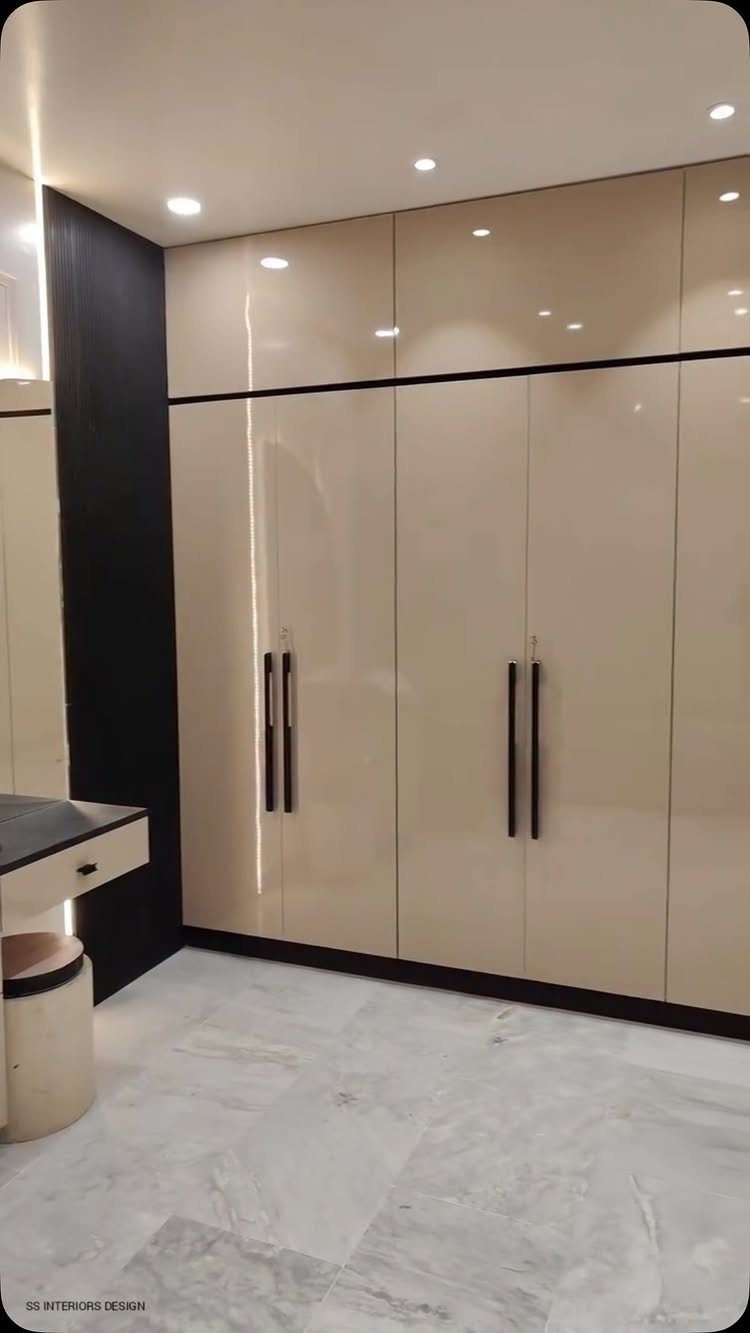 Glossy beige built-in wardrobes with black handles in a room with marble floors.