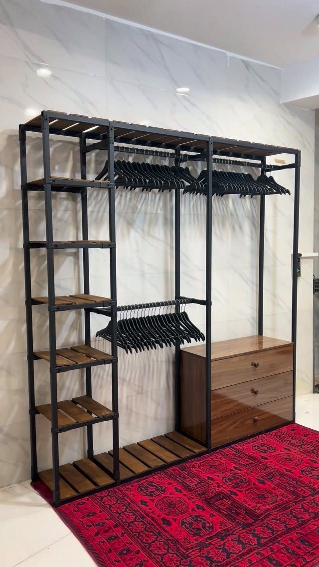 Industrial black metal clothing rack with wooden shelves, hanging rods, and a wooden dresser unit.