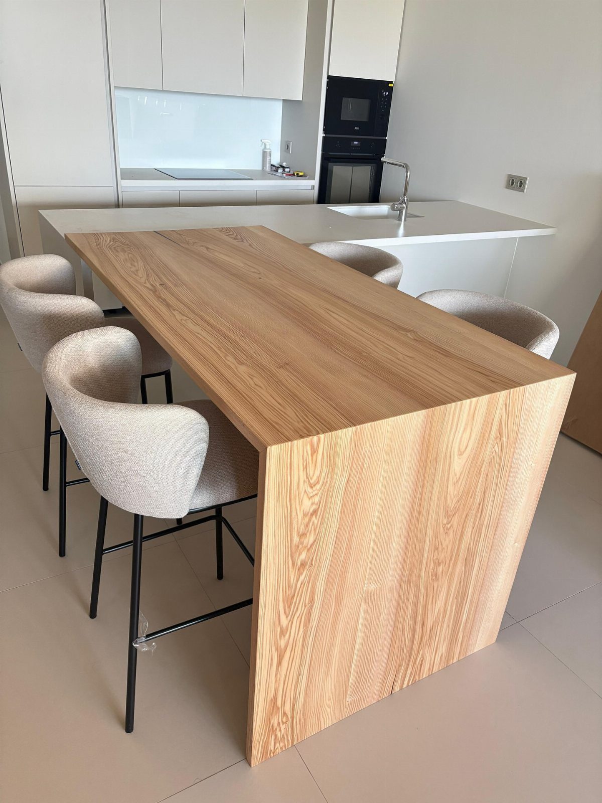 A wooden breakfast bar extension attached to a white kitchen island with four beige stools.