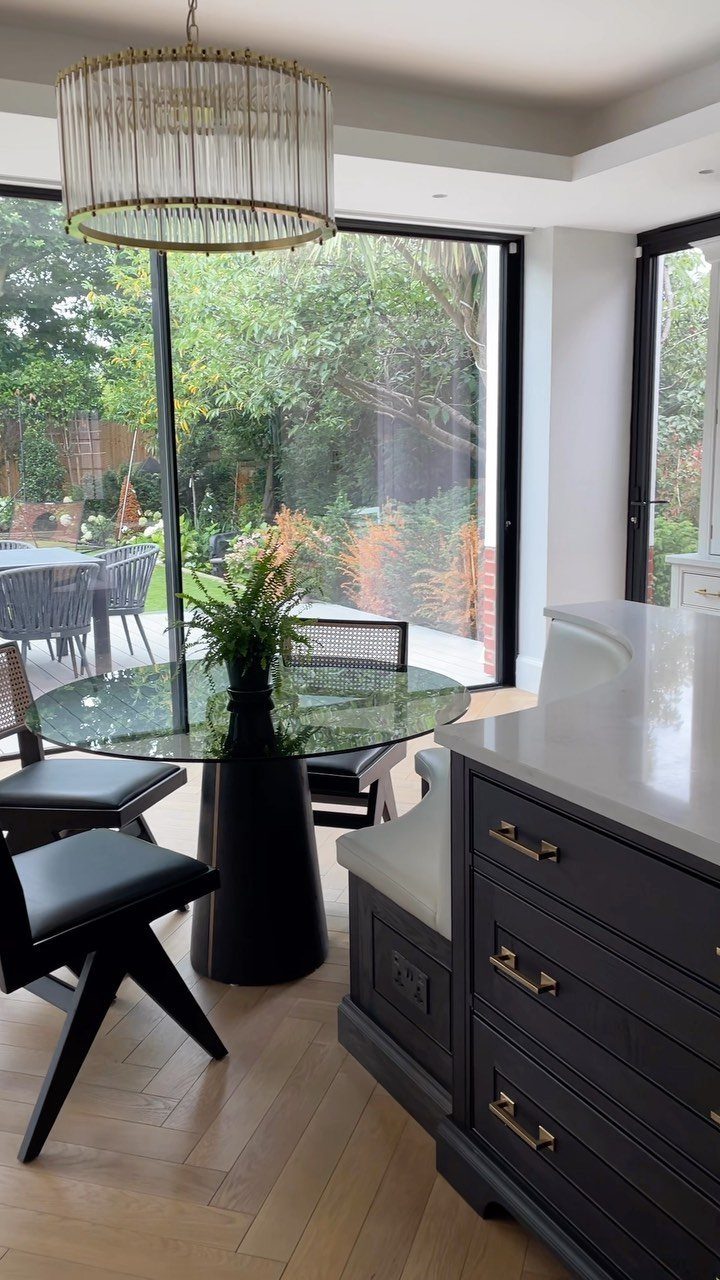A dark grey kitchen island featuring an integrated upholstered banquette seat and a glass dining table.