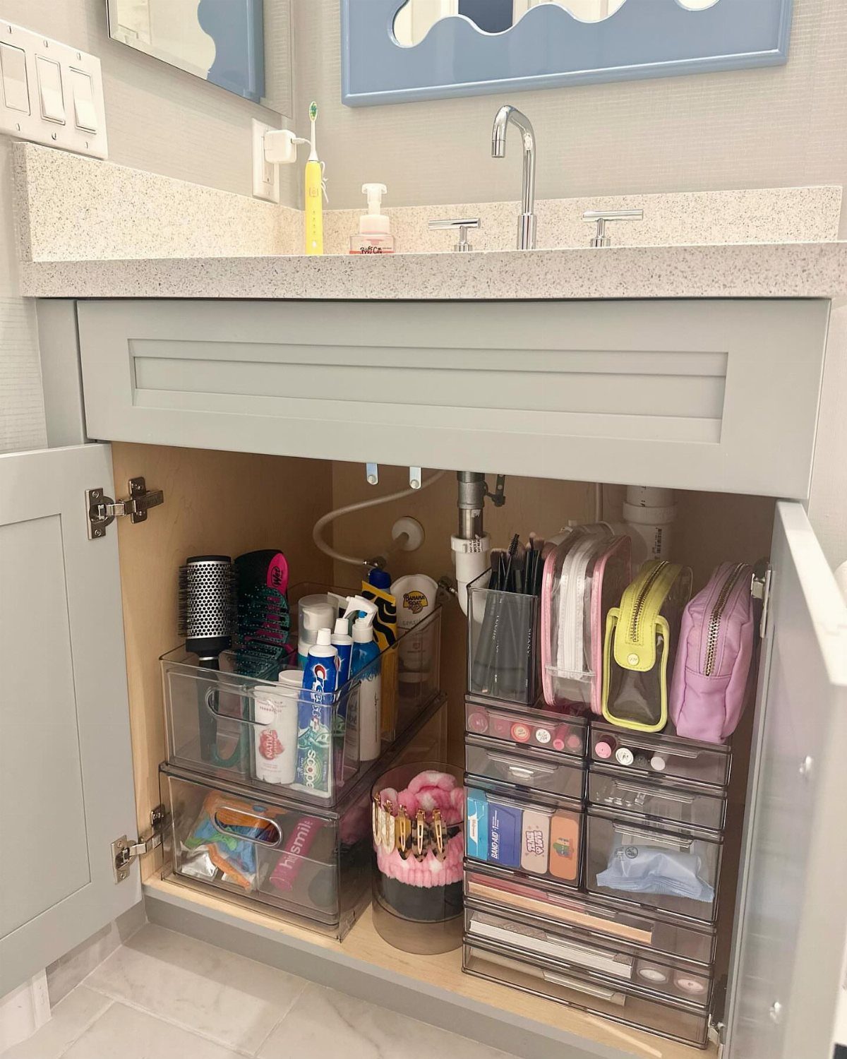 Organized clear plastic bins and drawers containing toiletries and beauty products inside a bathroom vanity cabinet.