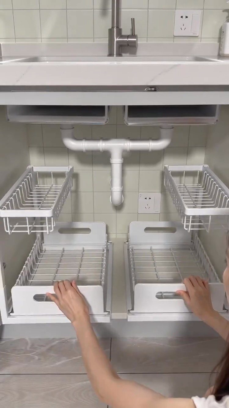 Hands pulling out white metal sliding drawer organizers from under a bathroom sink cabinet.
