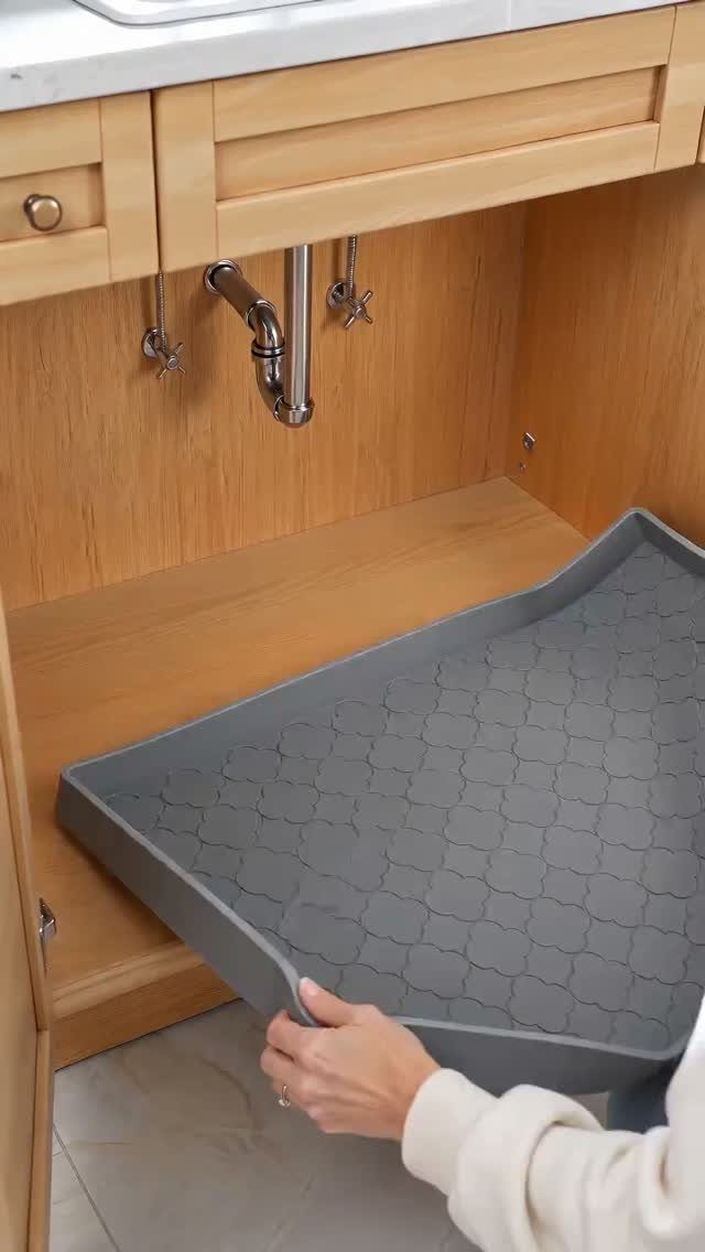 Hands placing a grey silicone tray into a wooden bathroom cabinet under the sink.