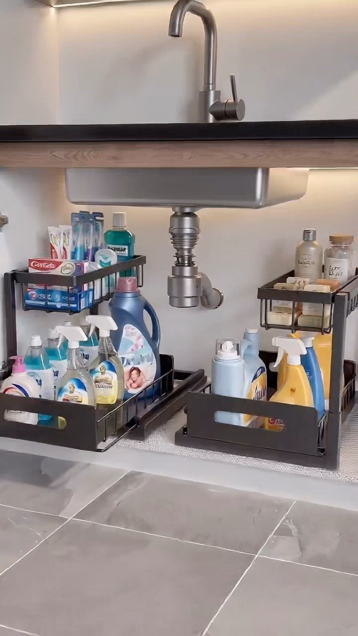 Black metal tiered organizers holding various cleaning supplies under a kitchen sink.