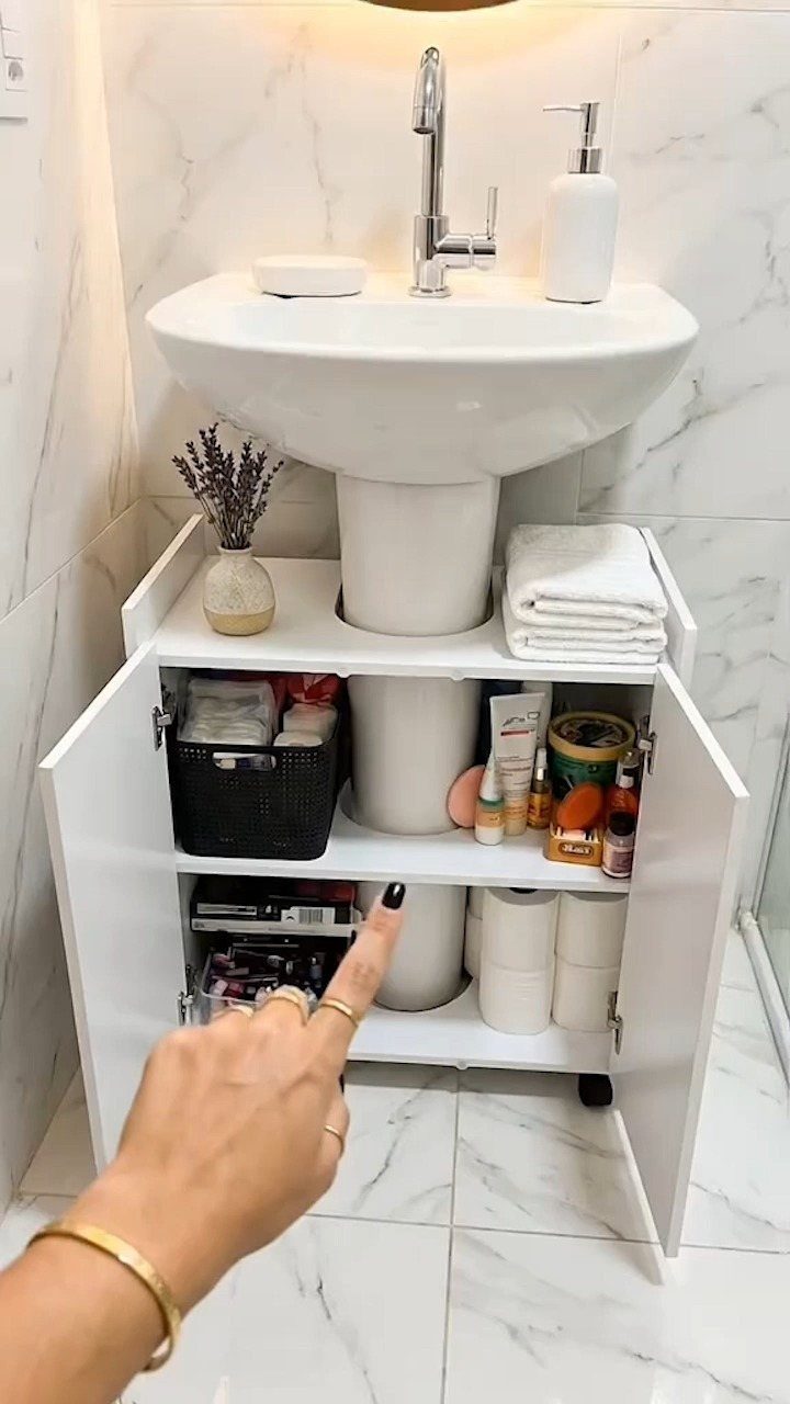 White storage cabinet organized with toiletries and baskets placed around a pedestal sink.