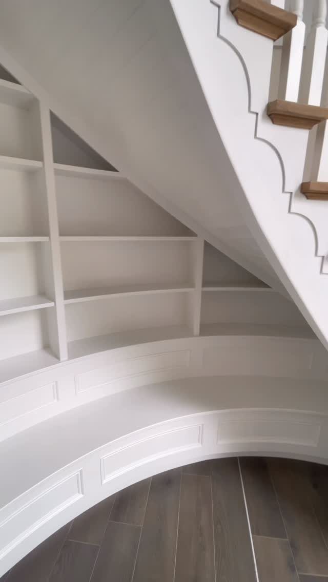 White built-in bookshelves installed within the triangular space underneath a staircase.