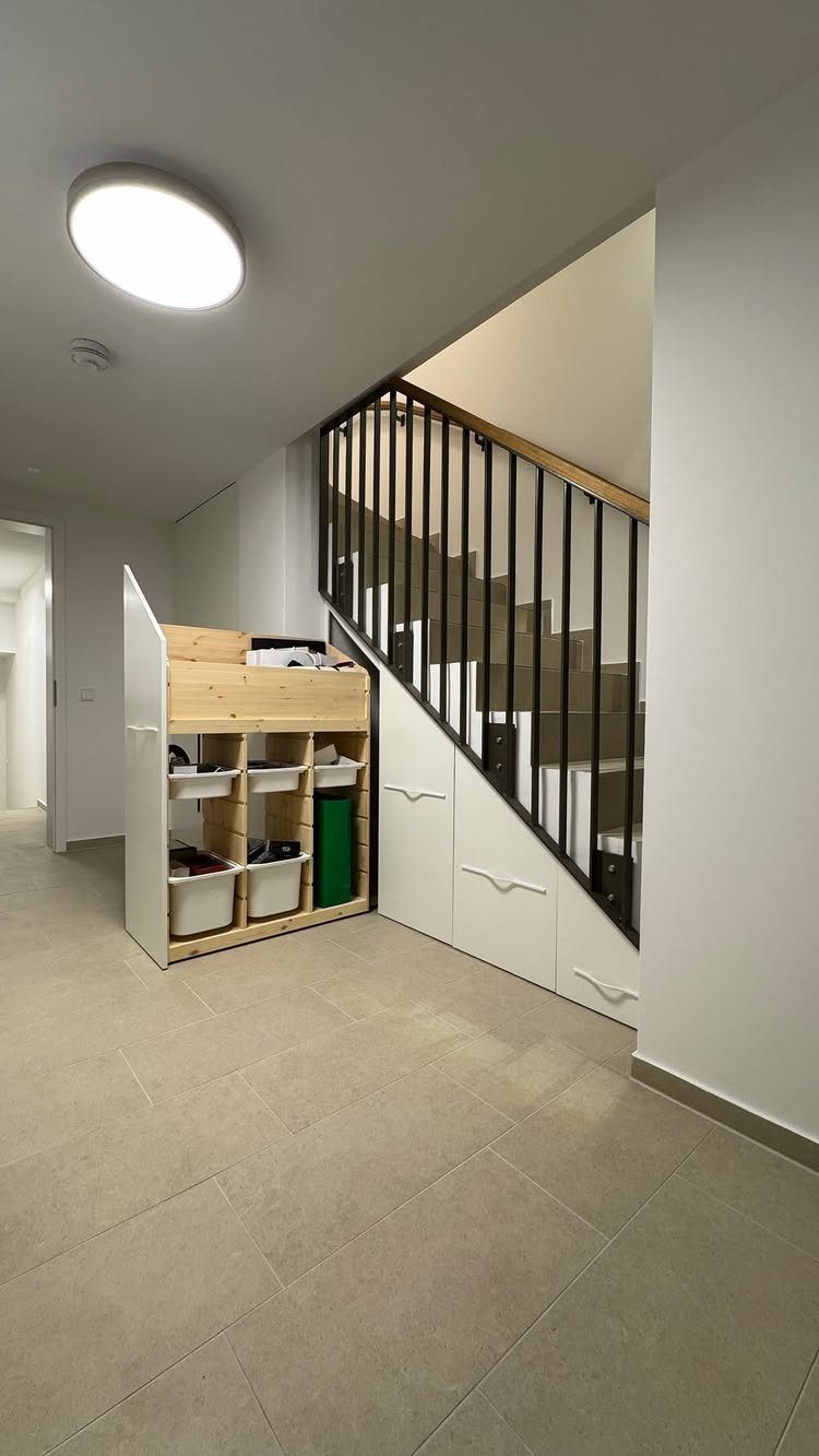 White and light wood storage cubbies and cabinets built under a staircase with black railings.