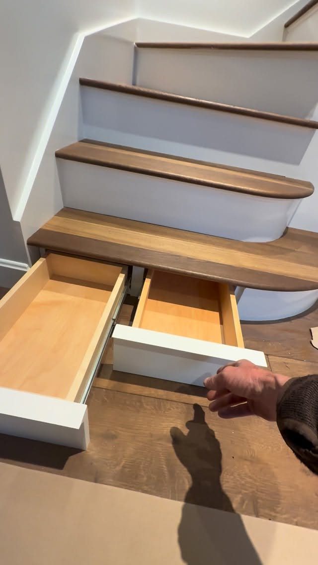 Two white wooden drawers pulled out from underneath a set of wooden stairs.