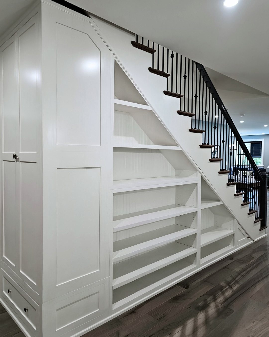 White built-in open shelving and a cabinet installed under a staircase with dark railings.