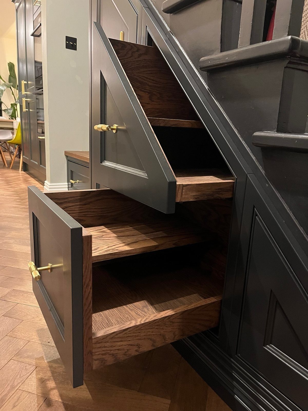 Two dark grey pull-out drawers with wooden interiors extended from under a staircase.