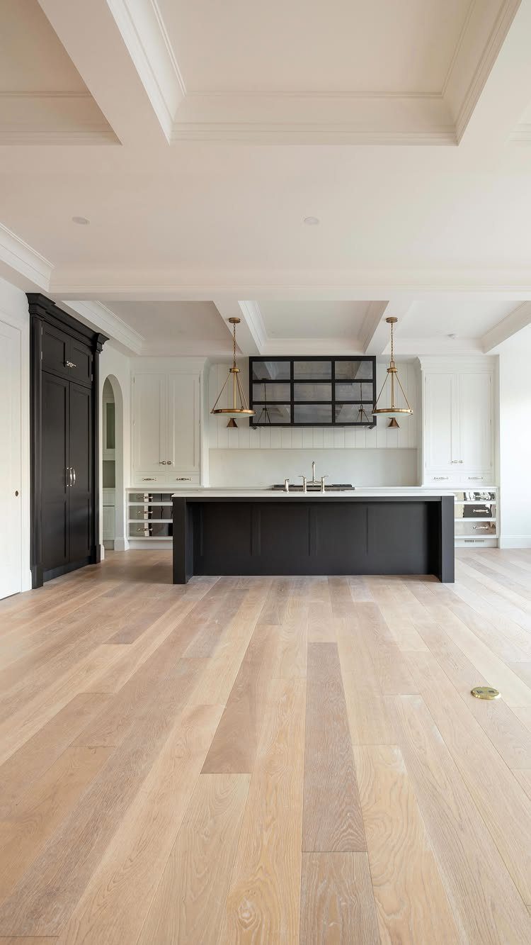 A modern kitchen with a large black island and white cabinetry on light wood floors.
