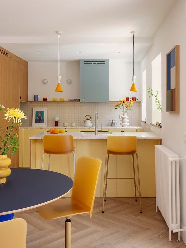 Yellow kitchen cabinets with a light blue upper cabinet and mustard yellow chairs.