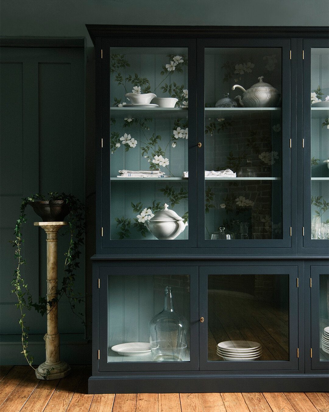 Dark navy blue wooden hutch with glass doors displaying white ceramic dishes and glassware.