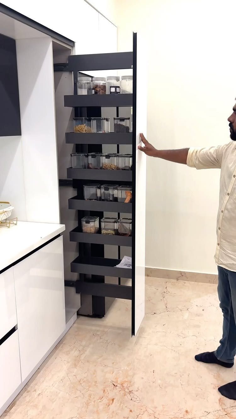 Vertical Pull Out Cabinet Kitchen: 7 Ideas That Fix Stiff Necks 4 A man pulling out a tall, black vertical pull-out kitchen cabinet filled with glass jars.